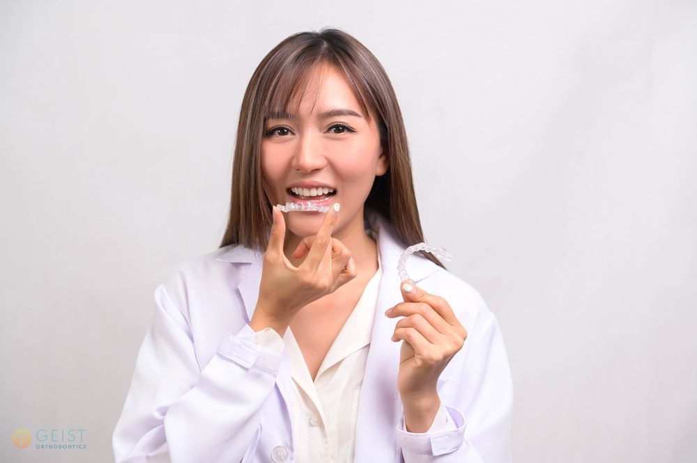 Smiling woman in a white outfit holding a clear aligner after understanding does insurance cover invisalign in Indianapolis, IN.