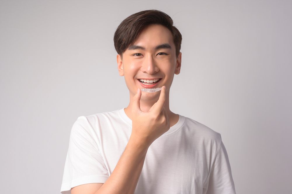 young smiling man holding invisalign aligners - Can Invisalign Fix Overbite in Indianapolis, IN