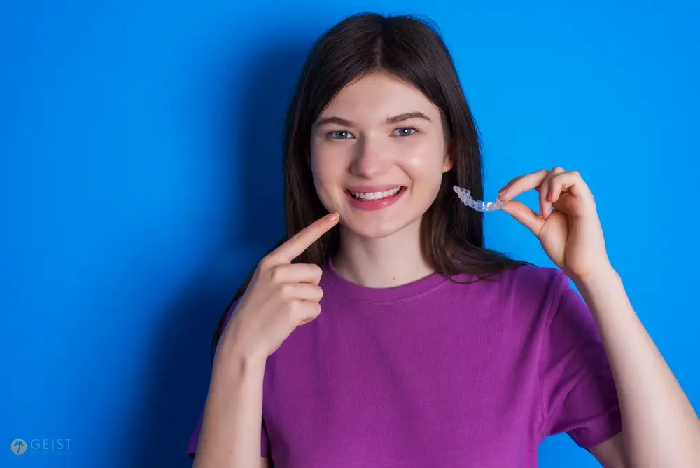 A cheerful woman pointing to her teeth with a bright smile, representing successful remedies for how to fix overbite in Indianapolis, IN.